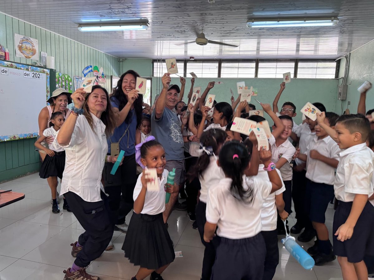 Schoolchildren and Foundation members raising cards and laughing in a classroom