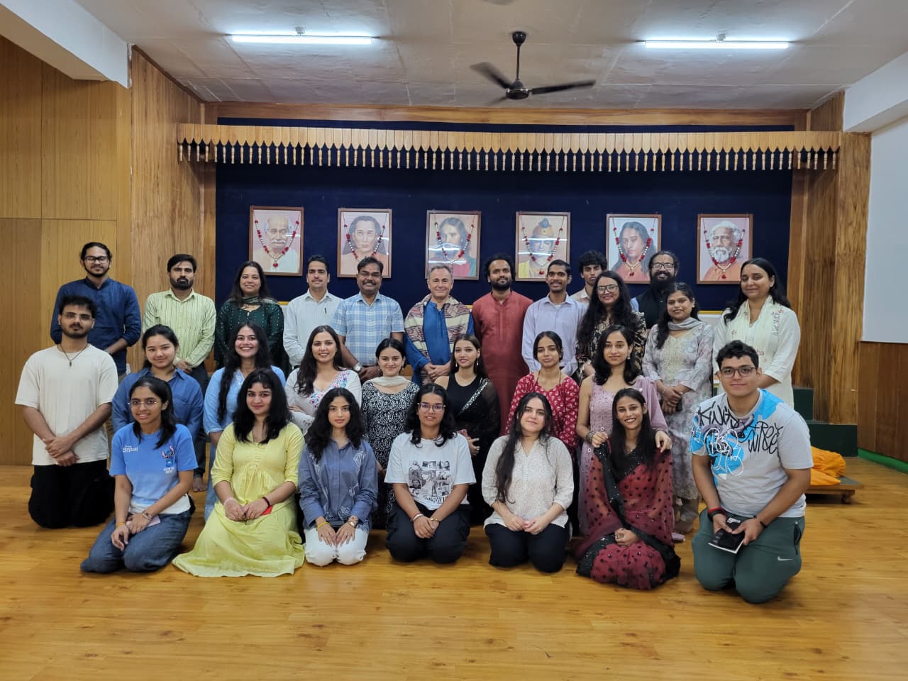 Sala contemplativa en Shoolini University: seis retratos del linaje de Kriya Yoga sobre lámparas encendidas, con personas pasando en primer plano