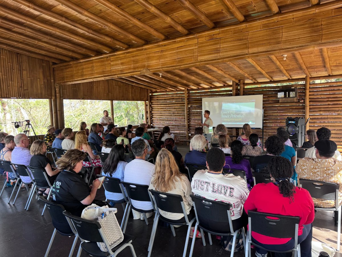 A speaker addressing a full room under a bamboo roof at the University for Peace