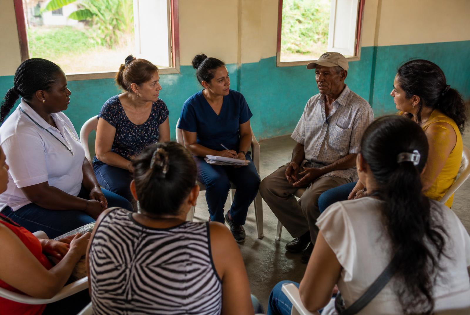 Community health workers and neighbours seated in a circle in a simple community hall
