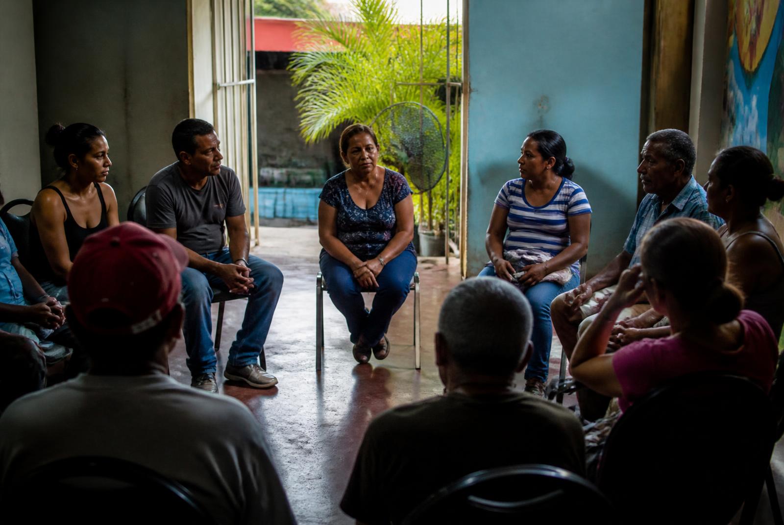 Adults seated in a circle in a modest neighbourhood room during a dialogue gathering