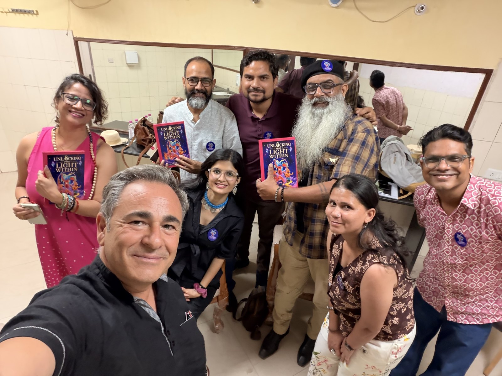 Luis Miguel Gallardo tirando uma selfie sorridente em grupo com oito amigos, três deles segurando exemplares do livro Unlocking Your Light Within.